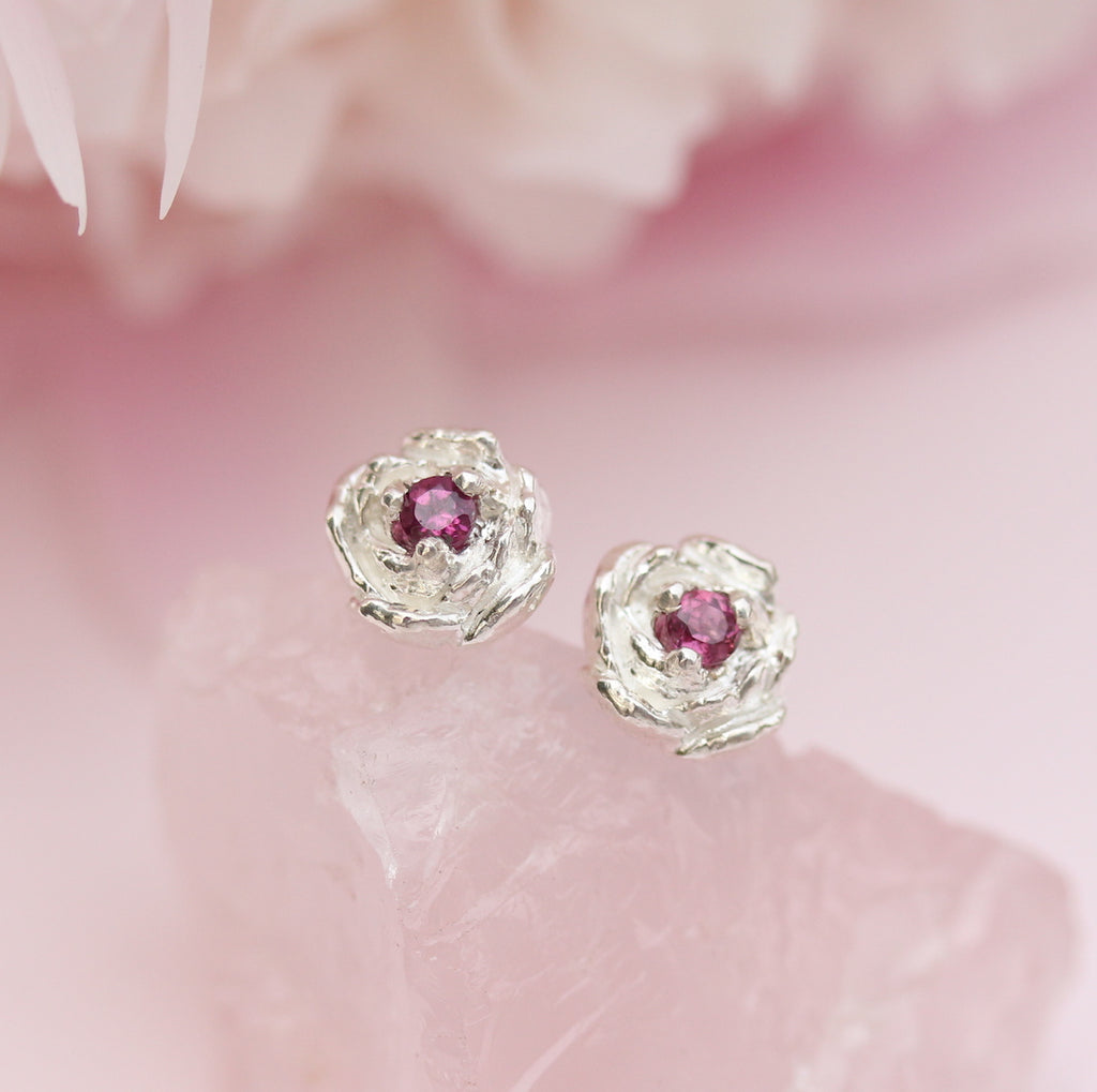 Peony stud earrings with garnet gemstones set in center on a pink backdrop