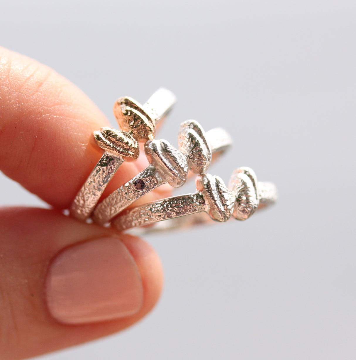 Gold and silver butterfly shell rings held by a hand on a light gray background