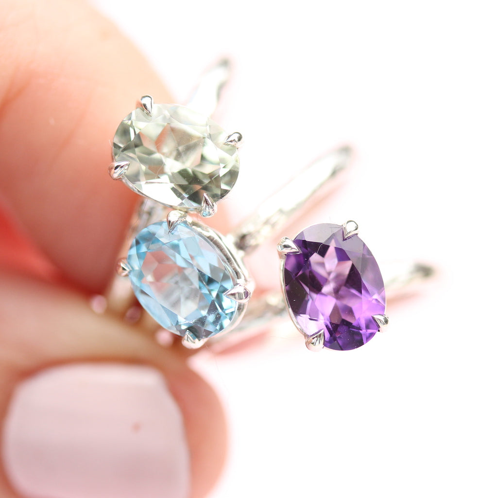 green amethyst, amethyst and blue topaz rings in hand