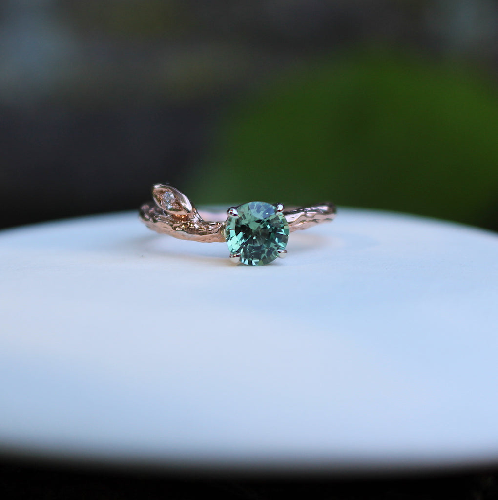 Branch and leaf rose gold ring with green sapphire on a plate