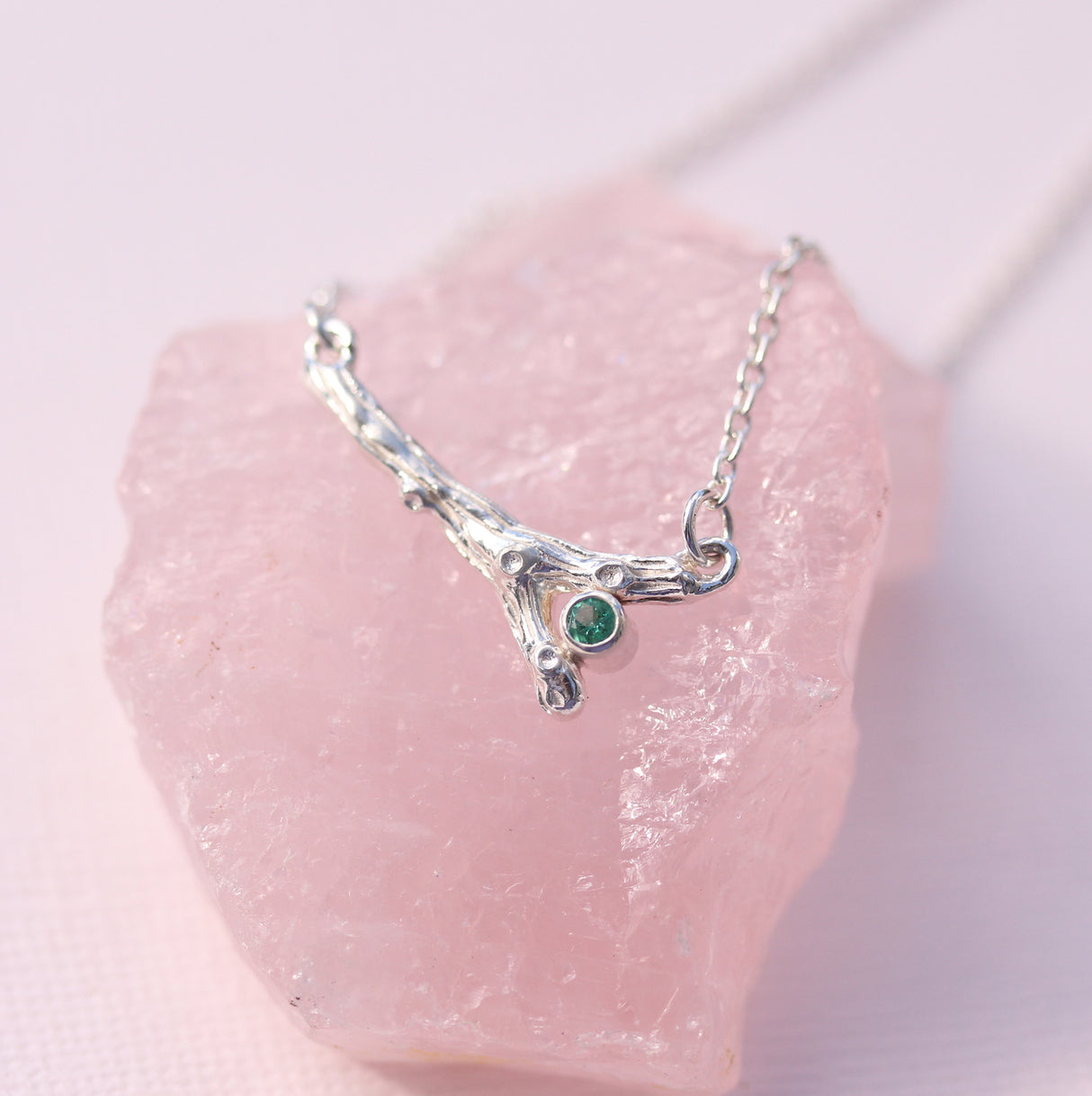 Silver necklace with a green gemstone on a pink crystal background