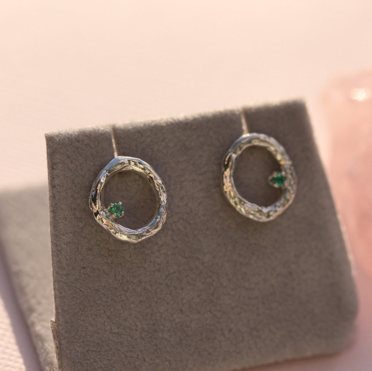 Silver earrings with green gemstones on a gray earring stand.