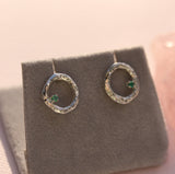 Silver earrings with green gemstones on a gray earring stand.