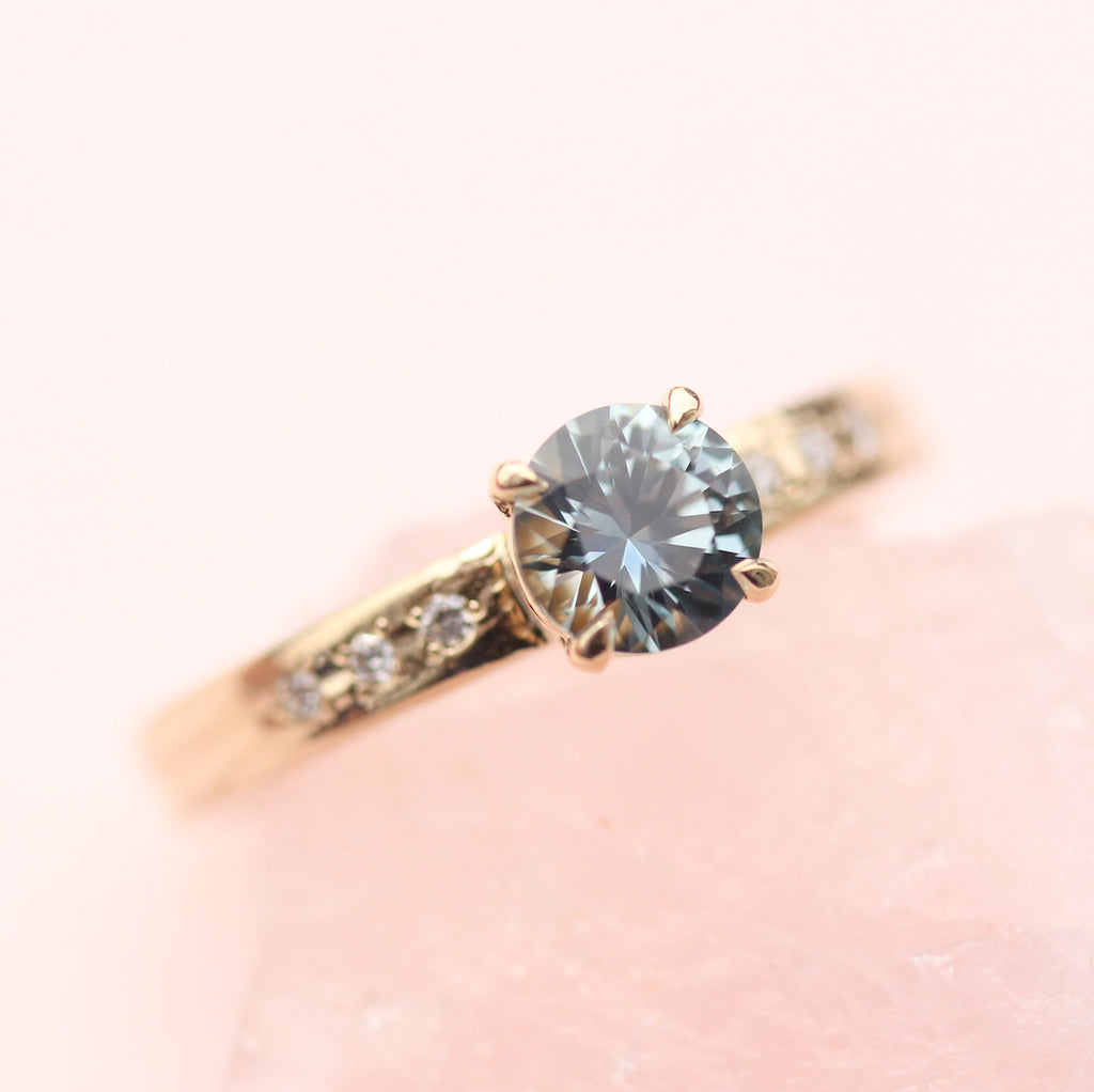 Teal sapphire ring resting on a pink rose quartz rock